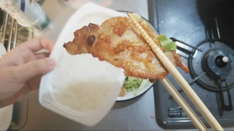 箸で持ち上げたクリスピージンジャーポークをご飯の上で寄りで見せる布団ちゃん