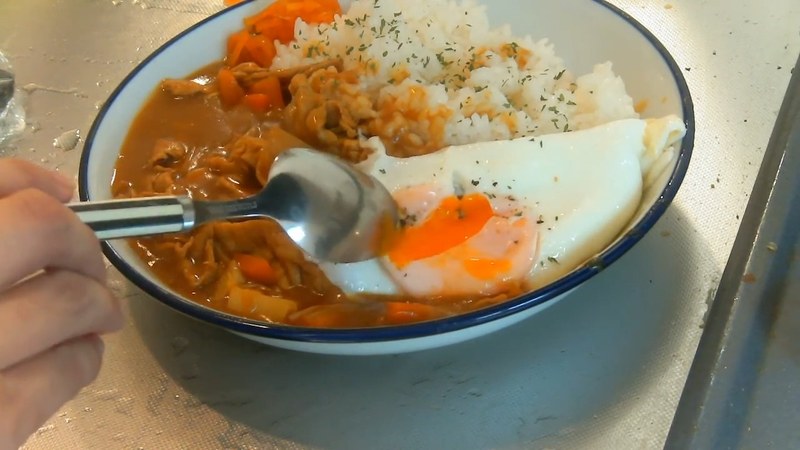 スプーンでカレーと卵をすくって食べる様子