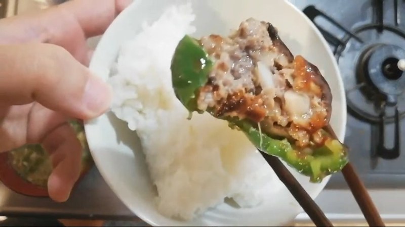 箸でピーマンの肉詰めを持ち上げ、断面を見せているところ