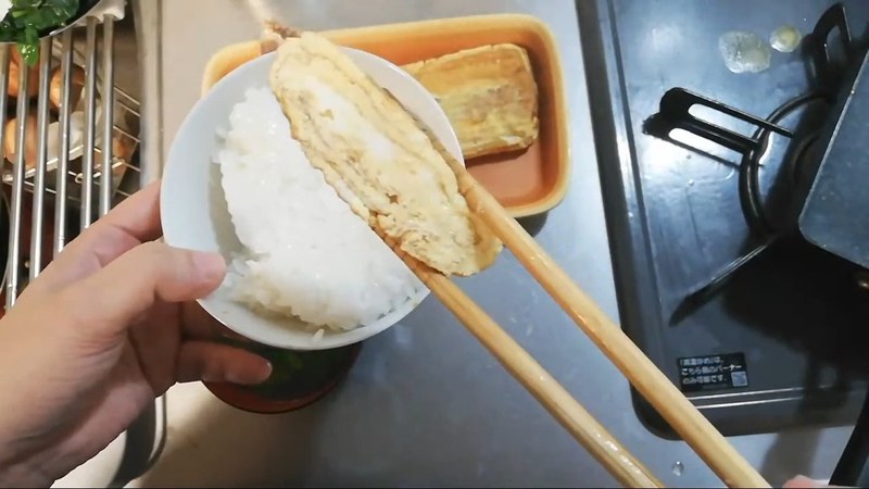 箸でだし巻き卵をご飯にのせようとしている